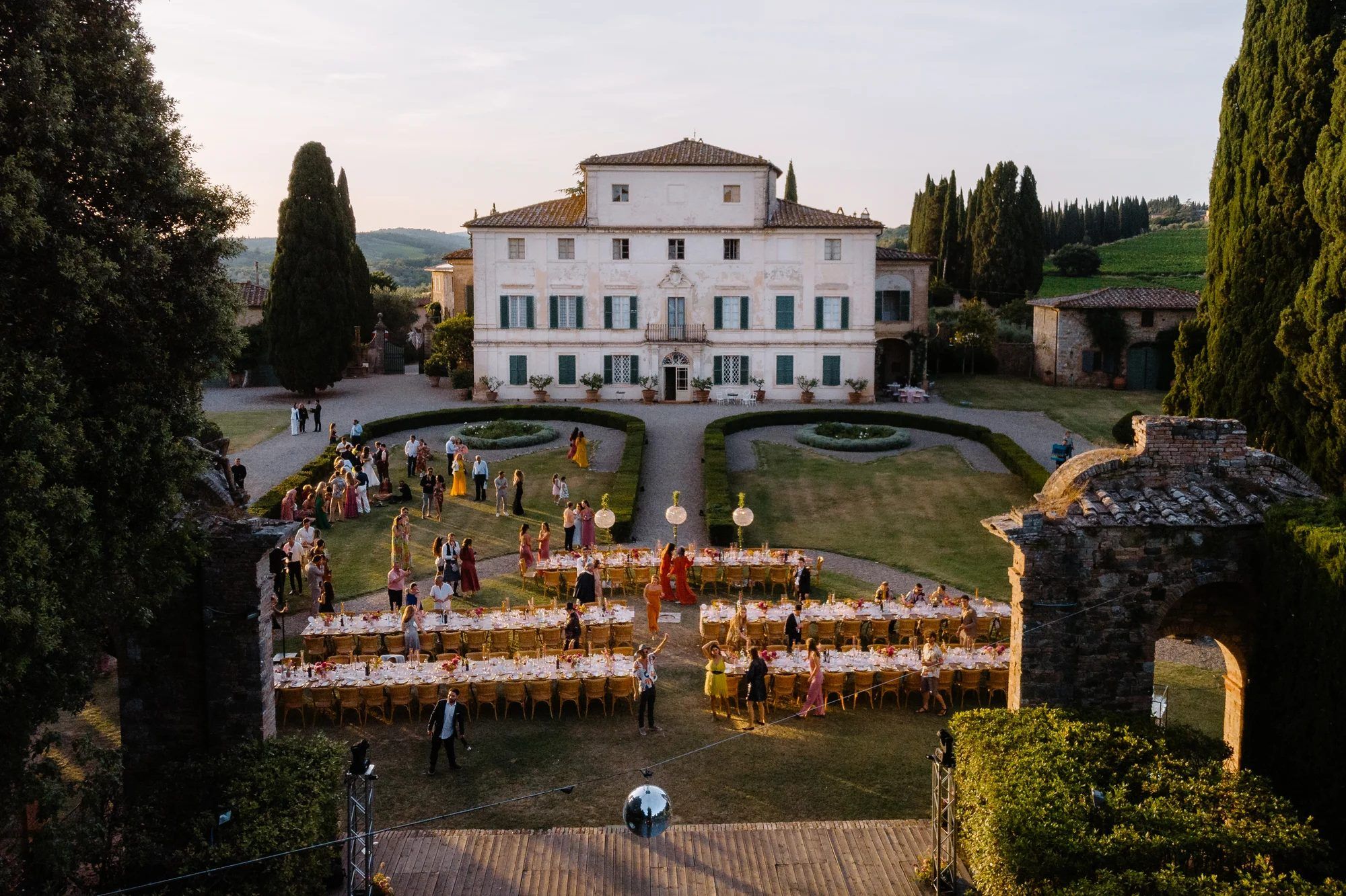 Long tables set for a celebration dinner in the gardens of a Tuscan villa at sunset
